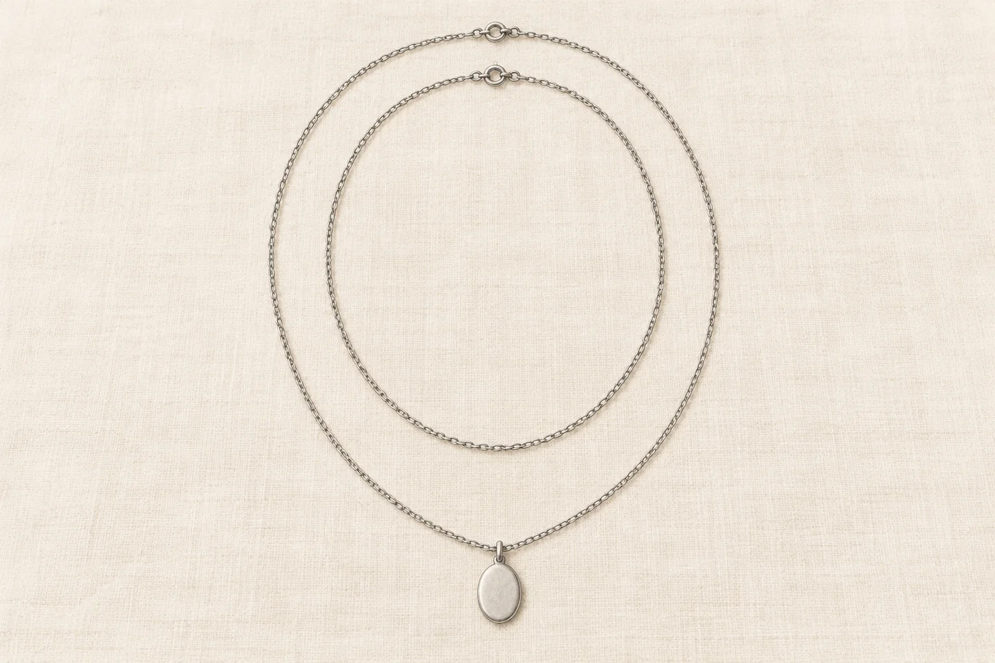 Illustration of two separate nested silver-coloured necklaces, with a pendant on the longer chain.